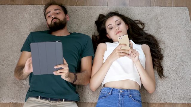 Young man and woman lying down on the floor of their new apartment. Top view footage