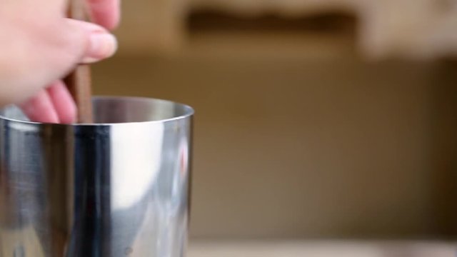 Hand using a wooden muddler to muddle ingredients for a cocktail in a silver shaker.
