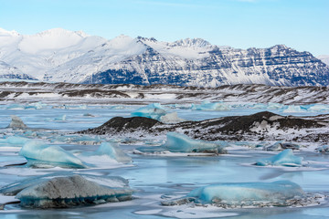 Fjallsarlon Glacial Lagoon, with snow, frozen glacial ice, and moraine in a mountainous environment