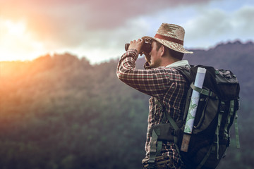 hiker with backpack standing looking through binoculars on the mountain - obrazy, fototapety, plakaty