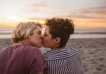 Loving young lesbian couple kissing on a beach at sunset