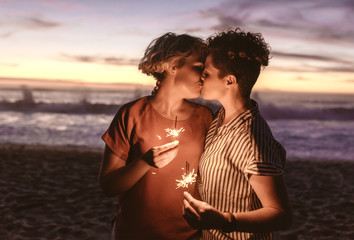 Romantic lesbian couple holding sparklers and kissing at the beach