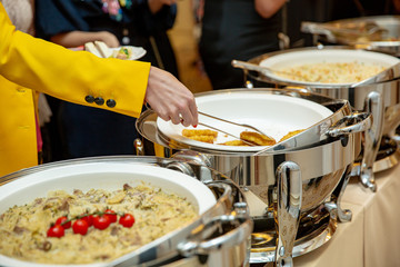 A group of tourists dine al fresco. A woman is laying food. Buffet.