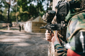 Fototapeta premium selective focus of paintball player in goggle mask and camouflage aiming by paintball gun outdoors