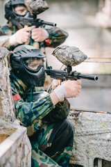 side view of concentrated paintball player in protective mask aiming with marker gun outdoors
