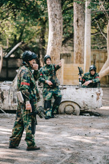 male paintballer in camouflage pointing by hand to his team near broken car outdoors