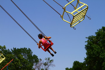 Girl on old chain carousel in park against blue sky, photo of people
