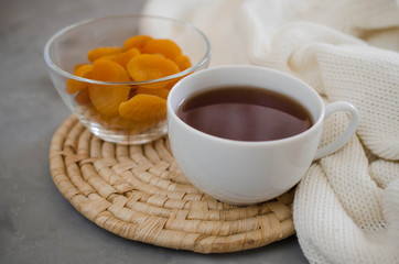 Cup of tea and dried apricots on a table, candles and knited blanket.