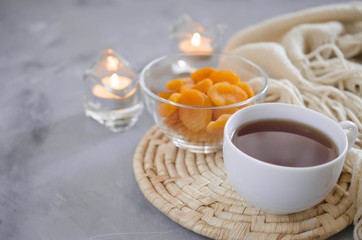 Cup of tea and dried apricots on a table, candles and knited blanket.