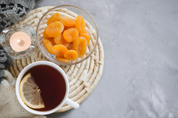Cup of tea and dried apricots on a table, candles and knited blanket.