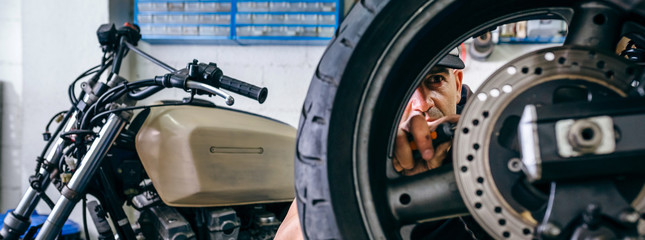 Mechanic fixing custom motorcycle wheel in his workshop. Selective focus on mechanic in background