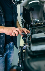 Obraz premium Fragment rąk mechanika naprawiającego niestandardowy motocykl w warsztacie