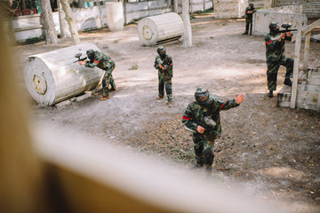 high angle view of paintball player in uniform pointing by hand to his team with markers guns outdoors