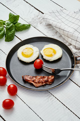 two delicious fried eggs and fried bacon arranged in a smiling face in a pan on a white kitchen table