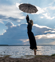 Beautiful young girl in black dress with umbrella dancing by the lake