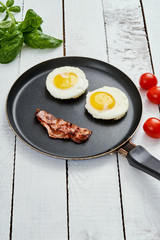 two delicious fried eggs and fried bacon arranged in a smiling face in a pan on a white kitchen table