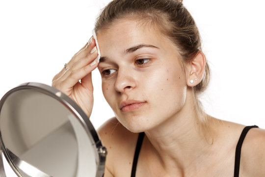 Young woman cleaning her face with wet cotton pade on white background