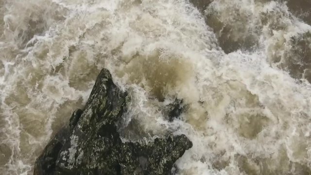 Overhead aerial of a strange shaped boulder in a turbulent river. Slow motion. The Rio Abanico on the Amazonian slopes of the Andes, Morona Santiago province, Ecuador, after heavy rain.