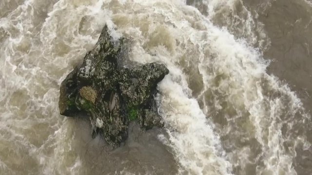 Overhead aerial of a strange shaped boulder in a turbulent river. Slow motion. The Rio Abanico on the Amazonian slopes of the Andes, Morona Santiago province, Ecuador, after heavy rain.