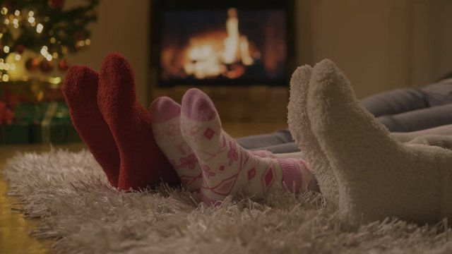 Low angle of 3 pairs of feet with Christmas socks in front of the fireplace