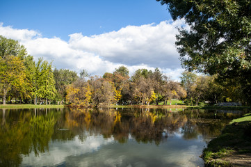 Beautiful autumn park with colorful trees and leaves and reflection in artificial ponds.