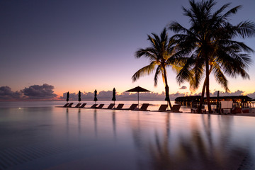 Beautiful poolside and sunset sky. Luxurious tropical beach landscape, deck chairs and loungers and water reflection.