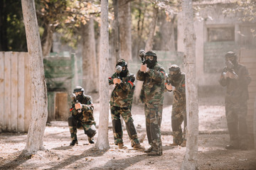 selective focus of paintball team in uniform and protective masks aiming by paintball guns outdoors
