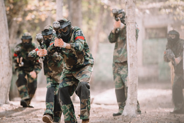 Fototapeta premium paintball team in uniform and protective masks aiming by paintball guns outdoors