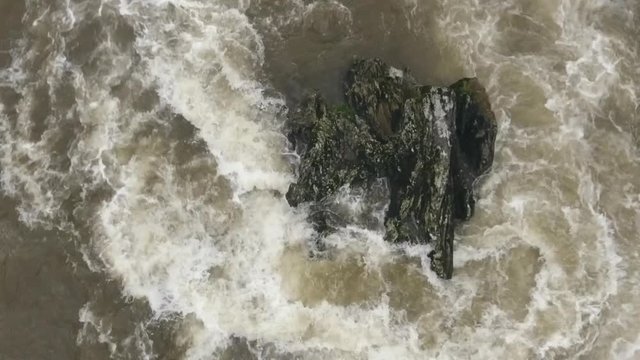 Overhead aerial of a strange shaped boulder in a turbulent river. Slow motion. The Rio Abanico on the Amazonian slopes of the Andes, Morona Santiago province, Ecuador, after heavy rain.