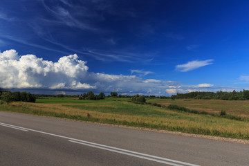 Road up hill with green grass field under white clouds and blue sky in summer day. Latgale. Latvia