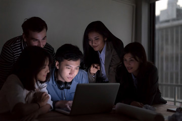 Smiling businesspeople are working with laptop  overtime late at nitgh. They are using laptop to search data. Setup studio shooting.