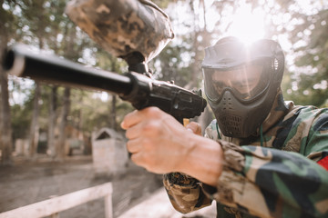 Fototapeta premium focused male paintball player in goggle mask and camouflage aiming by paintball gun outdoors