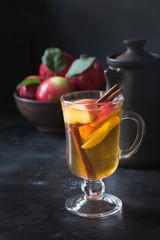 Glass of tea with lemon, spiced, sliced apple and cinnamon on black board. Autumn still life.