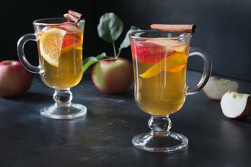 Glass of tea with lemon, spiced, sliced apple and cinnamon on black board. Autumn still life.
