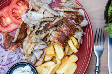 Griechisches Essen knusprige Döner Gyros Teller Portion mit Kartoffeln Pommes Frites und Zaziki Joghurt und roten zwiebeln 