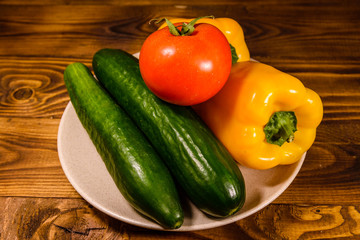 Ceramic plate with cucumbers, tomatoes and sweet pepper on wooden table