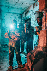 Obraz na płótnie Canvas paintball team in uniform and protective masks with paintball guns in abandoned building