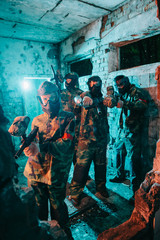 Fototapeta na wymiar paintball team in uniform and protective masks aiming by paintball guns at camera in abandoned building