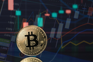 Bitcoin cryptocurrency coin token in gold with financial stock market charts in the background. Concept for digital currency trading and blockchain technology of the future.