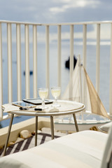 Working and traveling, busy luxurious lifestyle concept background. Shallow depth of field. Focus on white wine glasses on table, next to it are e book, cell phone and pencil. Ocean view from balcony.