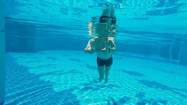 man shows thums up under the water in a pool