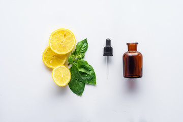 top view of bottle of natural herbal essential oil, dropper, lemon pieces and green leaves isolated on white