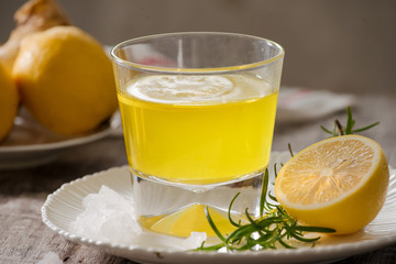 Ginger tea with lemon, ginger root and rosemarry on wooden background. Small glass transparent pitcher with hot drink. Seasonal beverages. Shallow DOF, selective focus, focus on top of pitcher.
