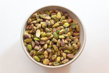 White ceramic bowl of pistachio nuts, centered, isolated on white, horizontal aspect