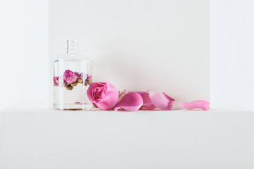 transparent bottle of natural herbal essential oil with pink roses on white surface
