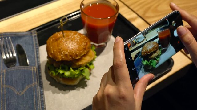 Girl makes a photo of burger and tomato juice on a smartphone in a cafe close up