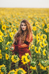 Naklejka na ściany i meble Young beautiful woman in a dress among blooming sunflowers. Agro-culture.