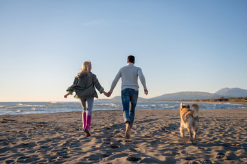 couple with dog having fun on beach on autmun day