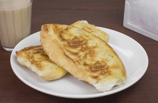 Popular Brazilian bread with melted butter called pão na chapa and a cup of hot coffee mixed with milk called média or pingado found in any bakery in wood background