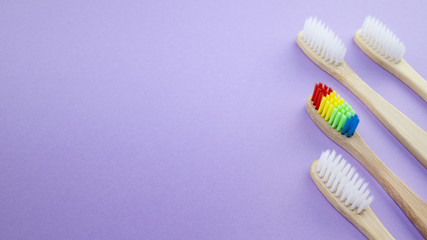 Fototapeta na wymiar White and rainbow wooden toothbrushes on violet or purple background. Concept of racism, social exclusion, depression or loneliness, social problems or illegal migration